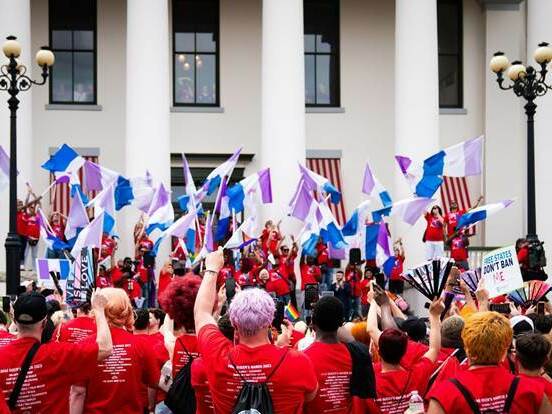 caption: Advocates outside Florida's historic Capitol wave drag pride flags during the Drag Queens March in 2023.