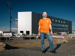 caption: Local activist and politician Thomas Loeb, 55, in front of the Tesla factory in Gruenheide on Oct. 26. Loeb is concerned that the factory poses a risk to the groundwater, forest and wildlife around it, and that Tesla has not been transparent about its manufacturing processes and developments.