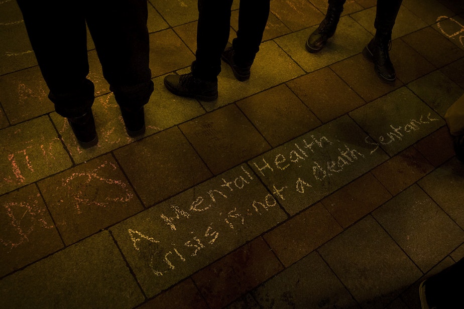 caption: 'A mental health crisis is not a death sentence' is shown written in chalk during a vigil in honor of a man who was shot and killed by two Seattle Police officers while in a crisis and holding a knife on Tuesday along Seattle's waterfront, on Wednesday, February 17, 2021, at Westlake Park in Seattle.