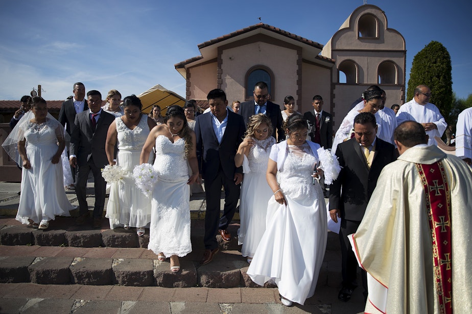 caption: Couples walk to have a group photograph taken on the steps of the church before a mass wedding ceremony with 23 couples on Sunday, June 2, 2019, at Our Lady of the Desert Church in Mattawa.