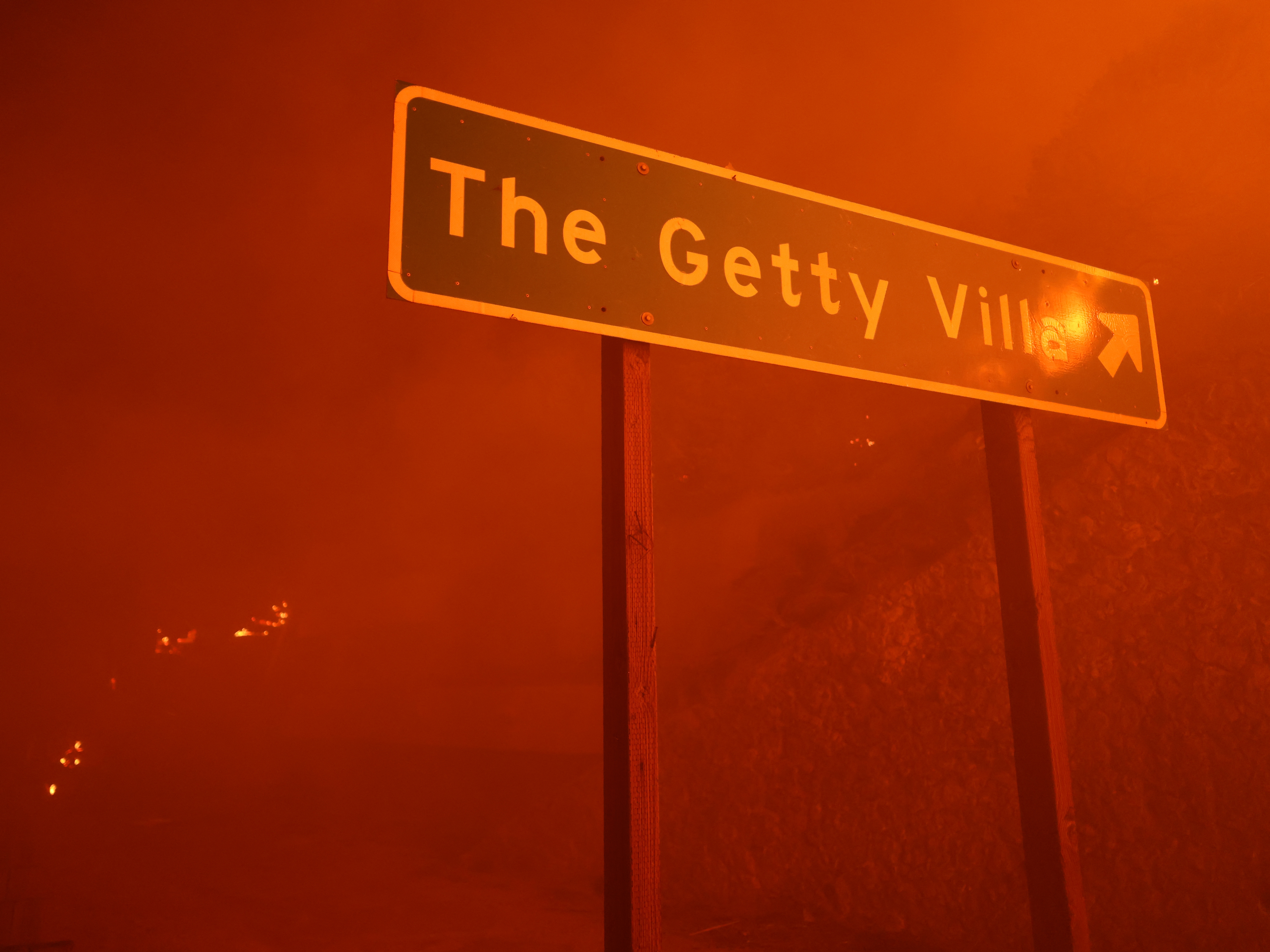 caption: A sign pointing to the Getty Villa art museum in engulfed in red smoke from the flames of the wind-driven Palisades Fire in Pacific Palisades, Calif., on Jan. 7, 2025.