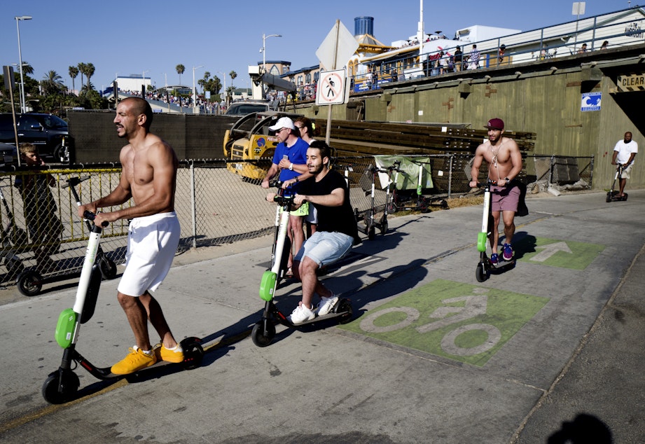 caption: In this July 1, 2018 photo people ride Lime and Bird scooters along the strand in Santa Monica, Calif. 