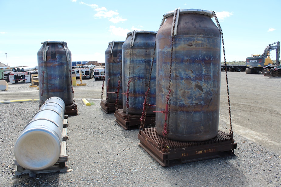 caption: Several low-activity waste containers sit at Hanford, while one high-level waste canister lays in the foreground.
