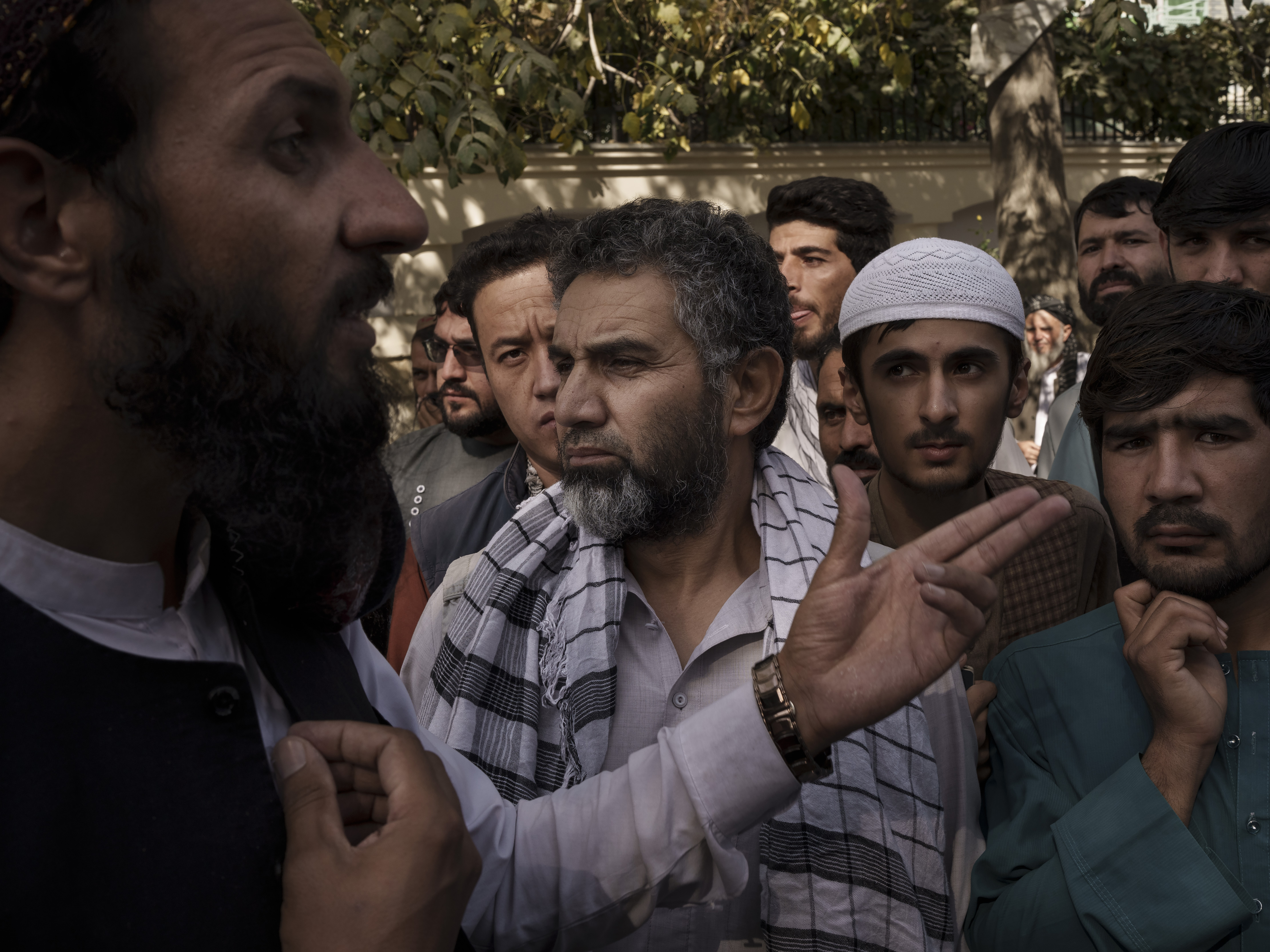 caption: A member of the Taliban, left, talks to Afghans gathering outside a government passport office recently re-opened in Kabul, on Oct. 6, 2021.