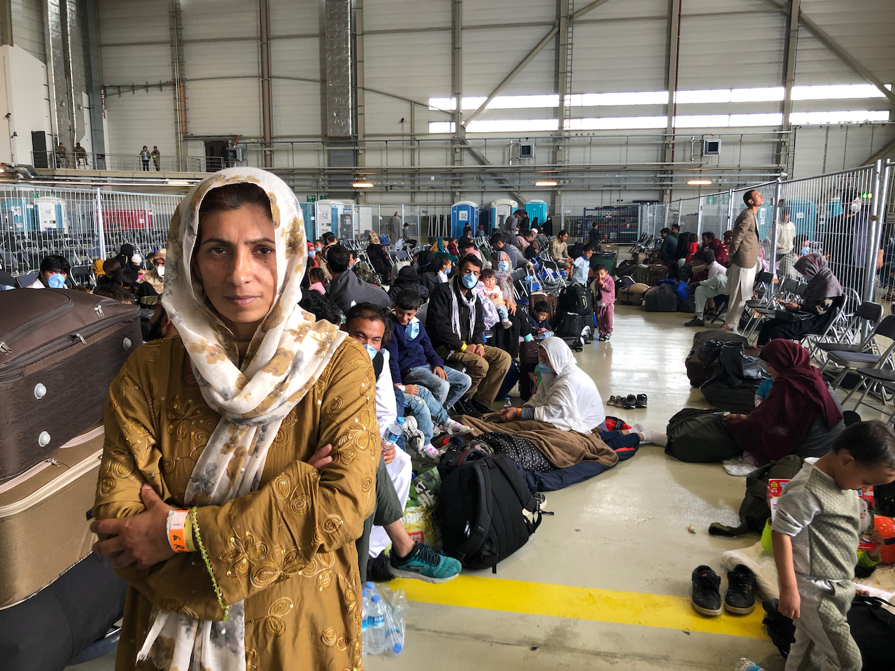 caption: Afghan evacuees wait for the next flight to the U.S. in a fenced-in enclosure in a hangar at Ramstein Air Base in Germany. More than 25,000 Afghans have traveled through Ramstein to get to the United States.