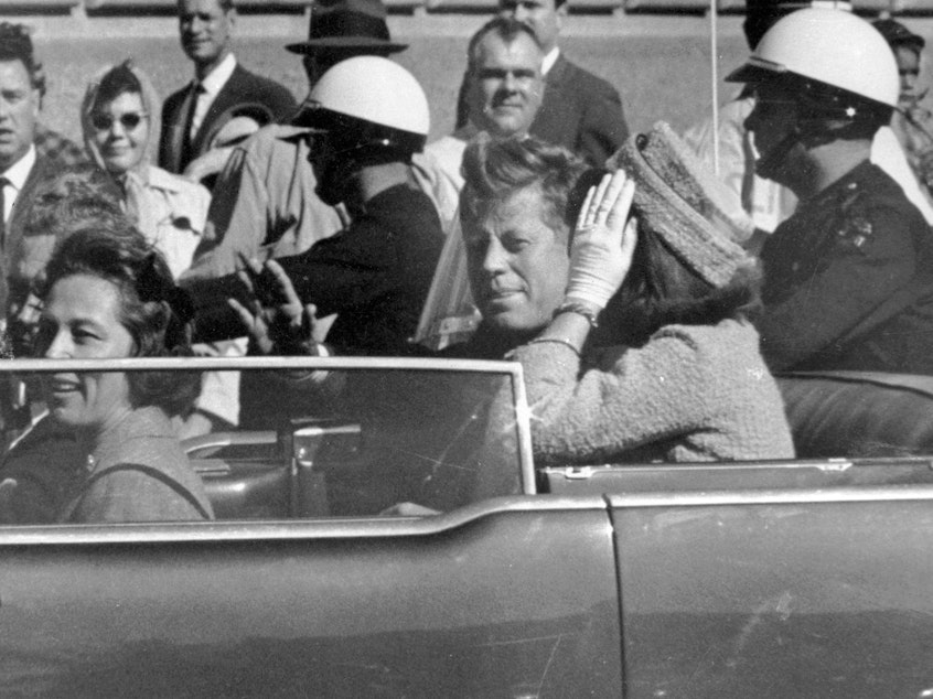caption: President John F. Kennedy and first lady Jacqueline Kennedy ride in the car in a motorcade in Dallas.