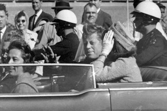 caption: President John F. Kennedy and first lady Jacqueline Kennedy ride in the car in a motorcade in Dallas.