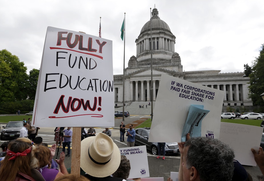 caption: Demonstrators stand on the steps of the Temple of Justice and in view of the Legislative Building as they advocate for more state spending on education prior to a hearing before the state Supreme Court on Sept. 3, 2014, in Olympia.