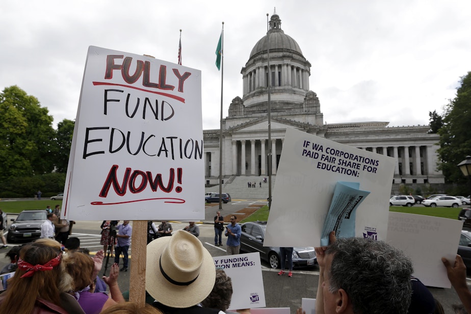 caption: Demonstrators stand on the steps of the Temple of Justice and in view of the Legislative Building as they advocate for more state spending on education prior to a hearing before the state Supreme Court on Sept. 3, 2014, in Olympia.