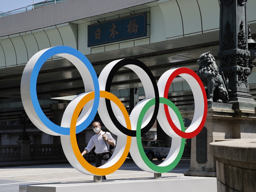 caption: A man wearing a face mask walks past the Olympic Rings ahead of the Tokyo 2020 Olympic Games. The Games are scheduled to begin this week in Japan despite a global rise in coronavirus cases.