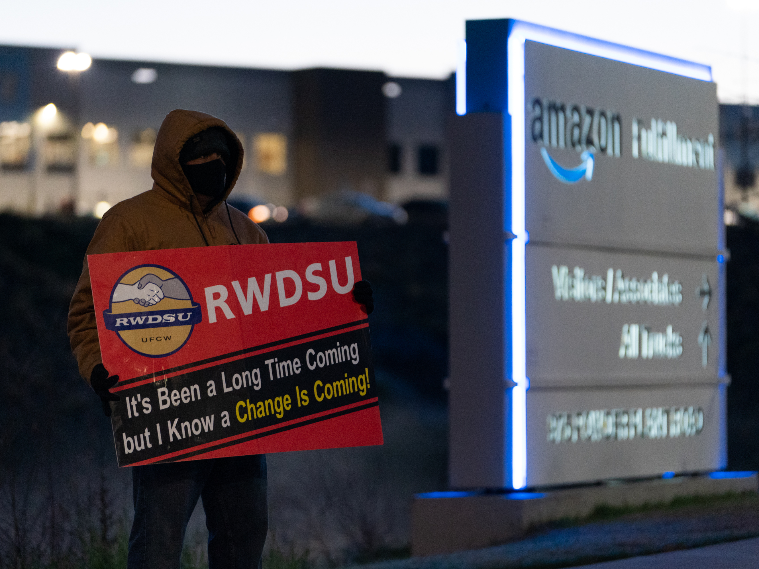 caption: A retail union representative holds a sign by the Amazon warehouse in Bessemer, Ala., during the first union election in March 2021.