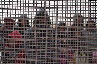 caption: Central American migrants stand at the U.S.-Mexico border fence in El Paso, Texas. The migrants turned themselves in to U.S. Border Patrol agents, seeking political asylum in the United States.