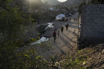 caption: Afuera del albergue Embajadores de Jesús en Tijuana, personas planean y esperan una nueva vida por delante.