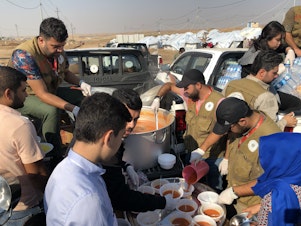 caption: Aid workers dish up rice and stew to refugees at the Gawilan camp in northern Iraq. The camp has accommodated nearly 2,000 new arrivals in the past month.