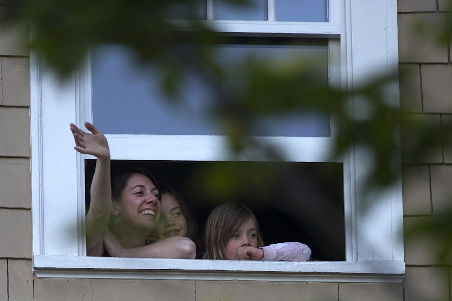 caption: Wallingford residents watch from a window as the Seattle Quarantine Parade passes by on Friday, May 8, 2020, in Seattle. 