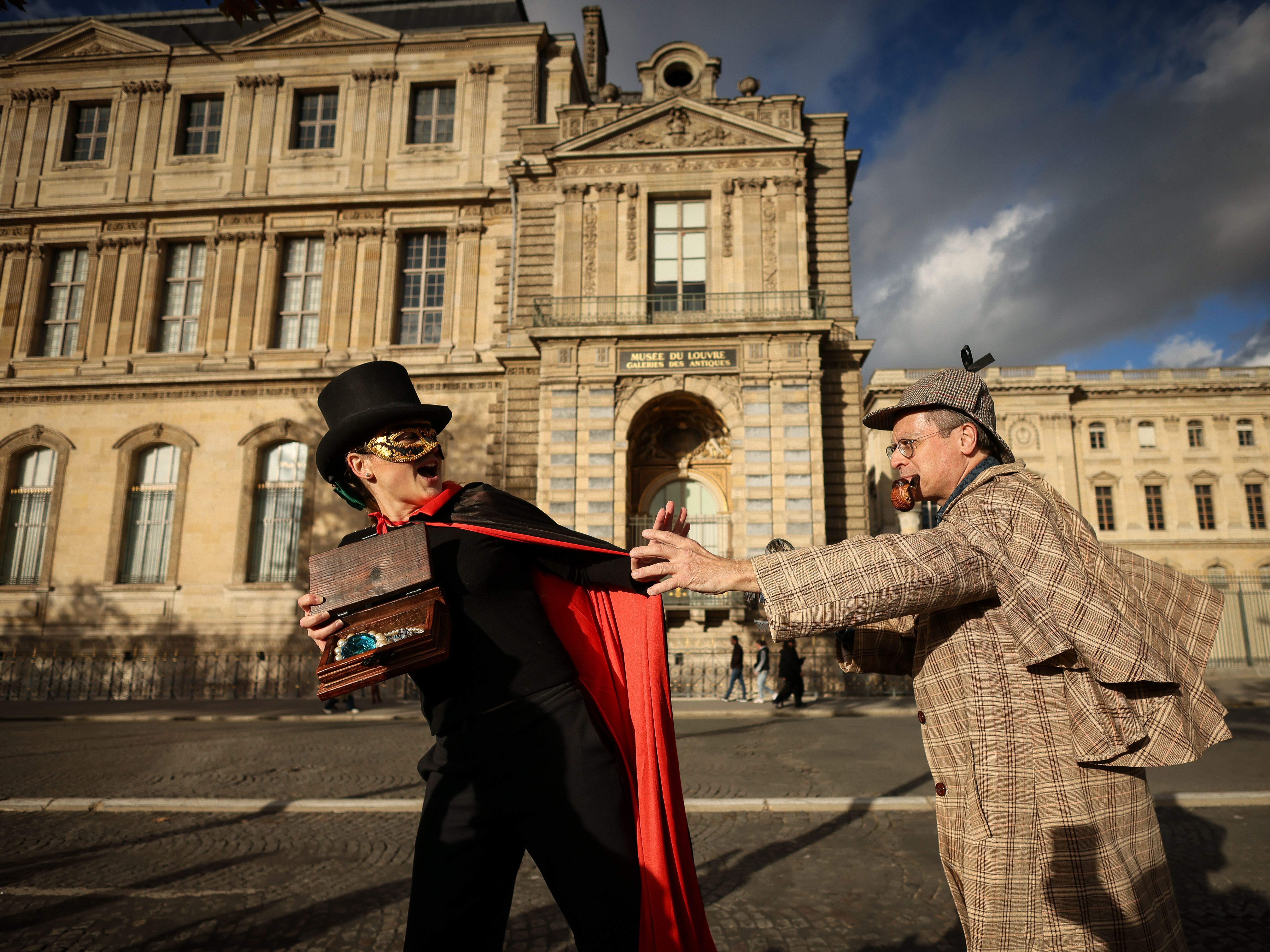 caption: Members of the Paris Holmes Society (Cercle Holmesien de Paris), Laurence Deloision, dressed like Arsène Lupin (left), and Thierry Gilibert, dressed like Sherlock Holmes, on Saturday stage the theft by the facade and the window where thieves entered the Louvre last Sunday.