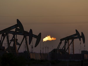 caption: A flare burns off methane and other hydrocarbons as oil pumpjacks operate in the Permian Basin in Midland, Texas, Oct. 12, 2021.
