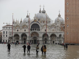 caption: People in front of St. Mark's Basilica wade in flood water in Venice on Wednesday.