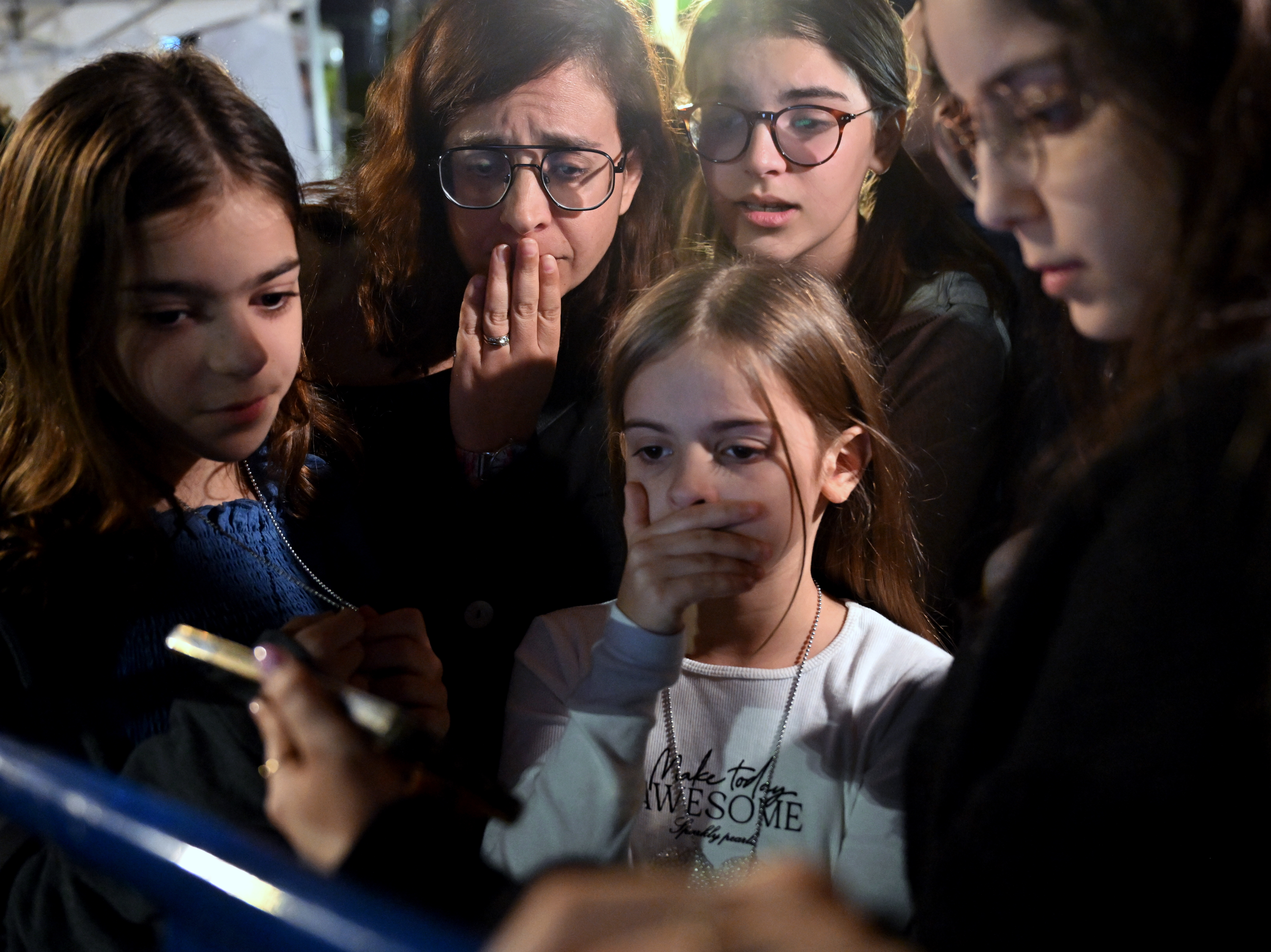 caption: A mother and her children react to the news that Hanna Katzir, who the Palestine Islamic Jihad claimed died in captivity, is among the 13 Israelis released. They are watching the news on their phone outside the Museum of Tel Aviv on Friday.