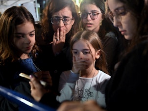 caption: A mother and her children react to the news that Hanna Katzir, who the Palestine Islamic Jihad claimed died in captivity, is among the 13 Israelis released. They are watching the news on their phone outside the Museum of Tel Aviv on Friday.