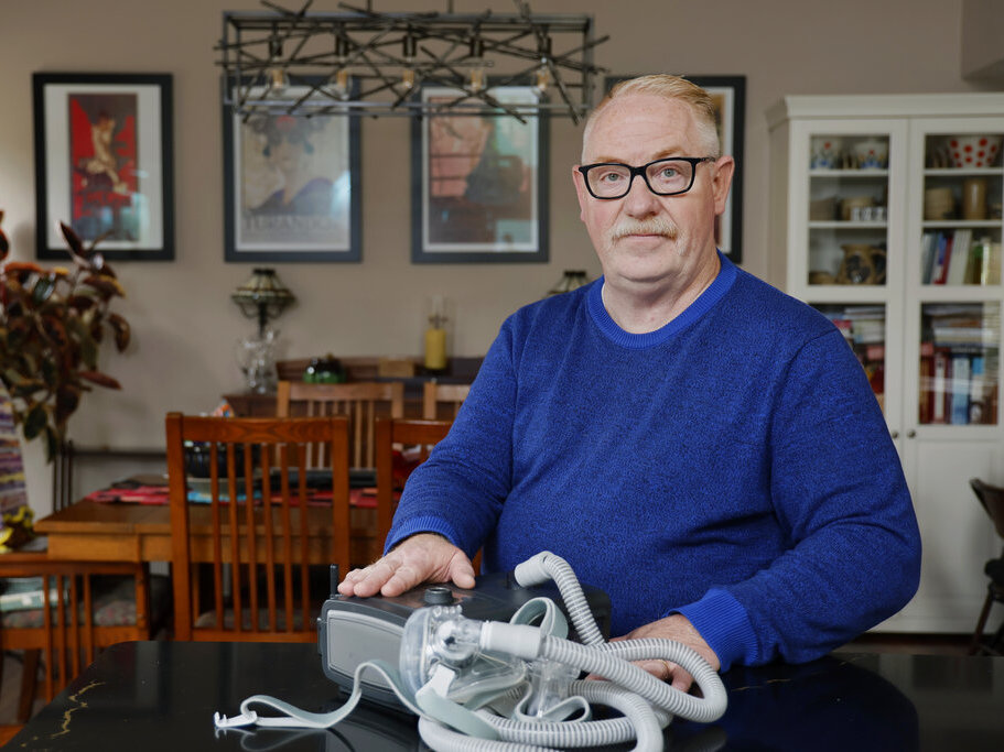 caption: Jeffrey Reed, who experienced persistent sinus infections and two bouts of pneumonia while using a Philips CPAP machine, poses with the device Oct. 20 at his home in Marysville, Ohio.