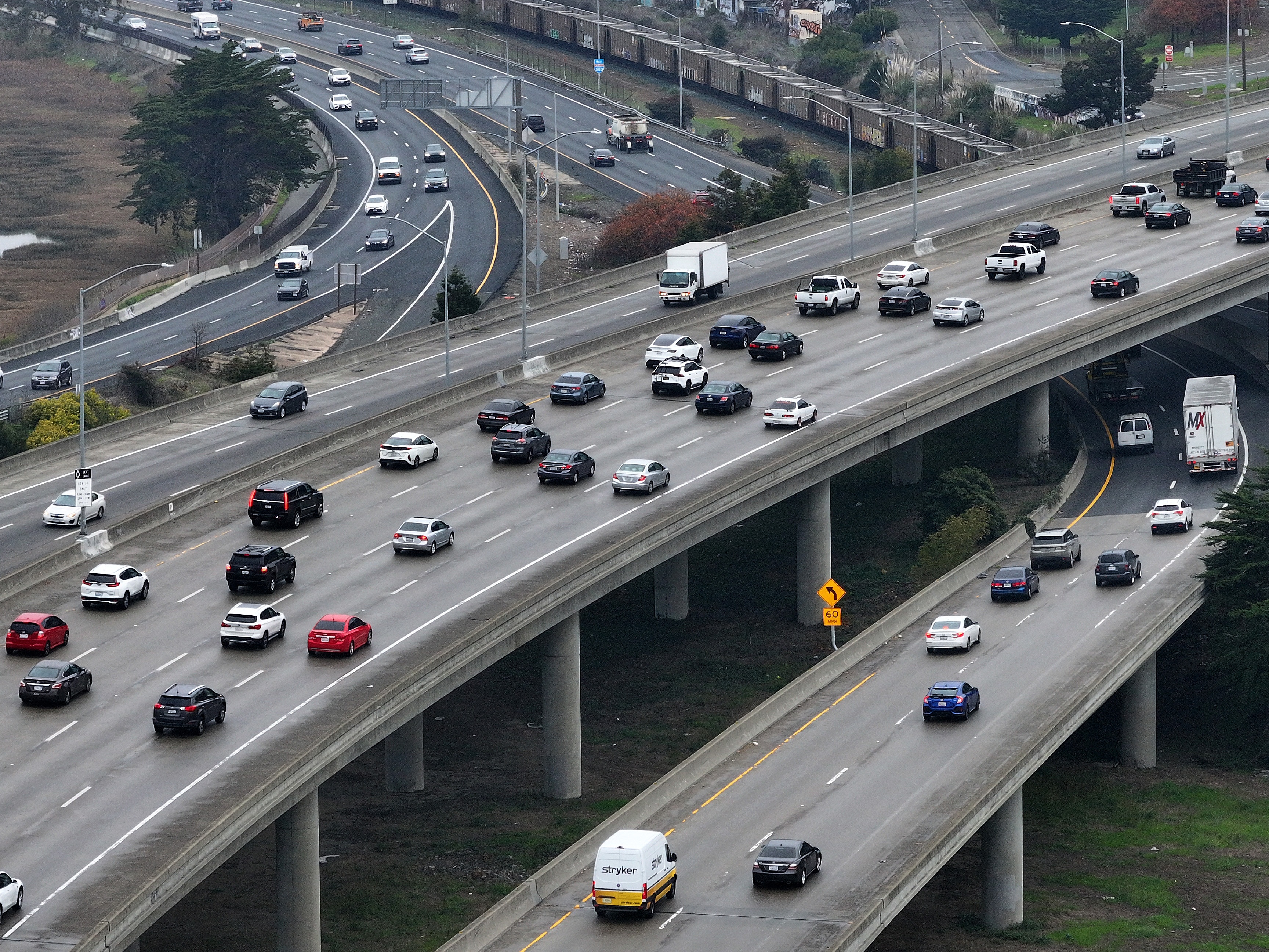 caption: In an aerial view, cars travel along Interstate 80 in Berkeley, Calif., on January 16, 2024. The regulations that require automakers to build more efficient, cleaner vehicles are being loosened under the Trump administration.