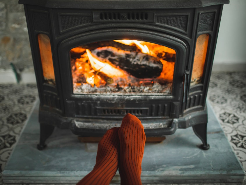 Feet in red socks by the burning fireplace. Family relaxes by warm fire and warming up theirs feet in woollen socks. Cozy atmosphere. Winter and Christmas holidays concept.