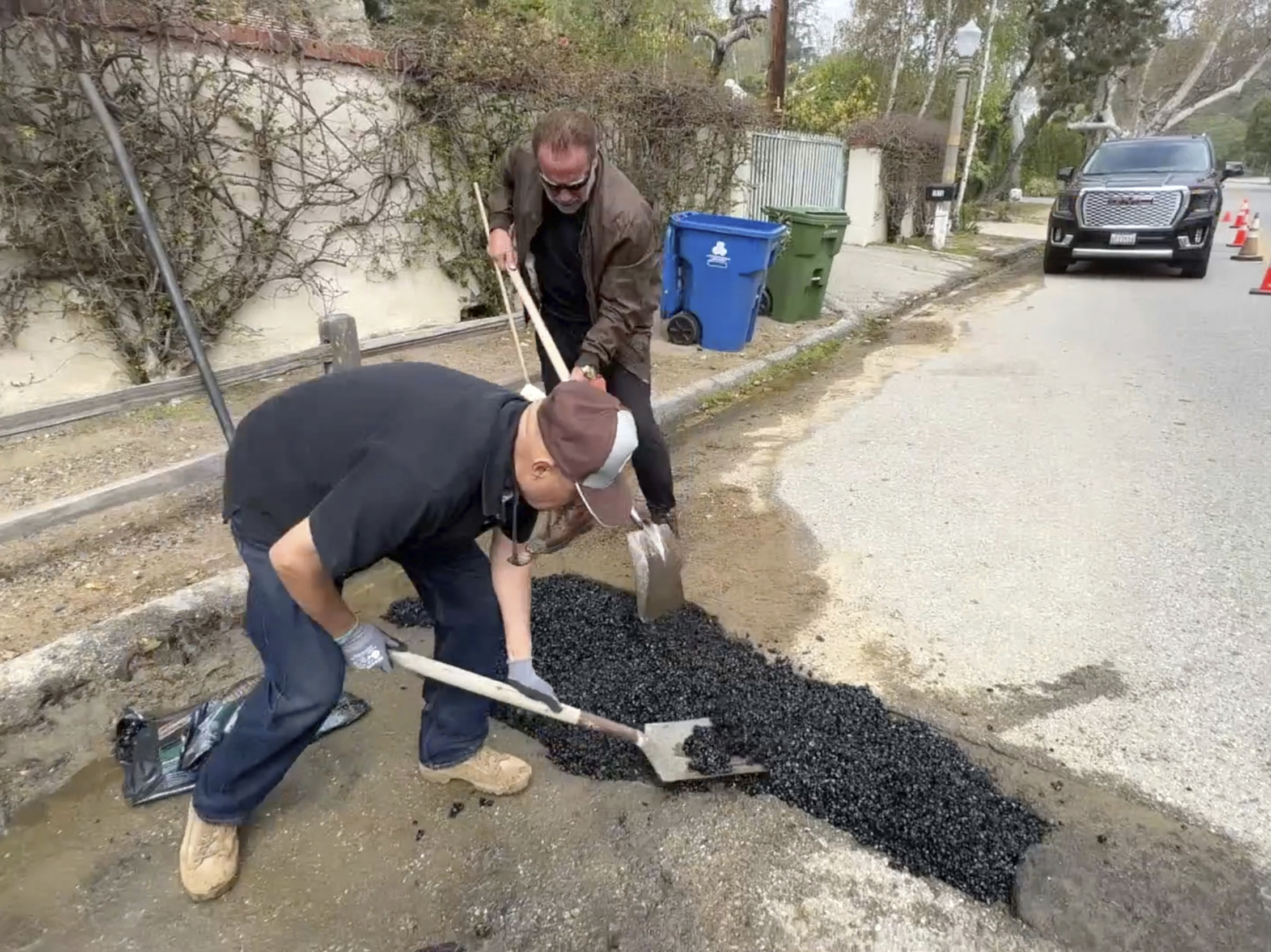 caption: This video still image provided by Arnold Schwarzenegger's office, shows the former California governor (center back) repairing a pothole on a street in his Los Angeles neighborhood on Tuesday.