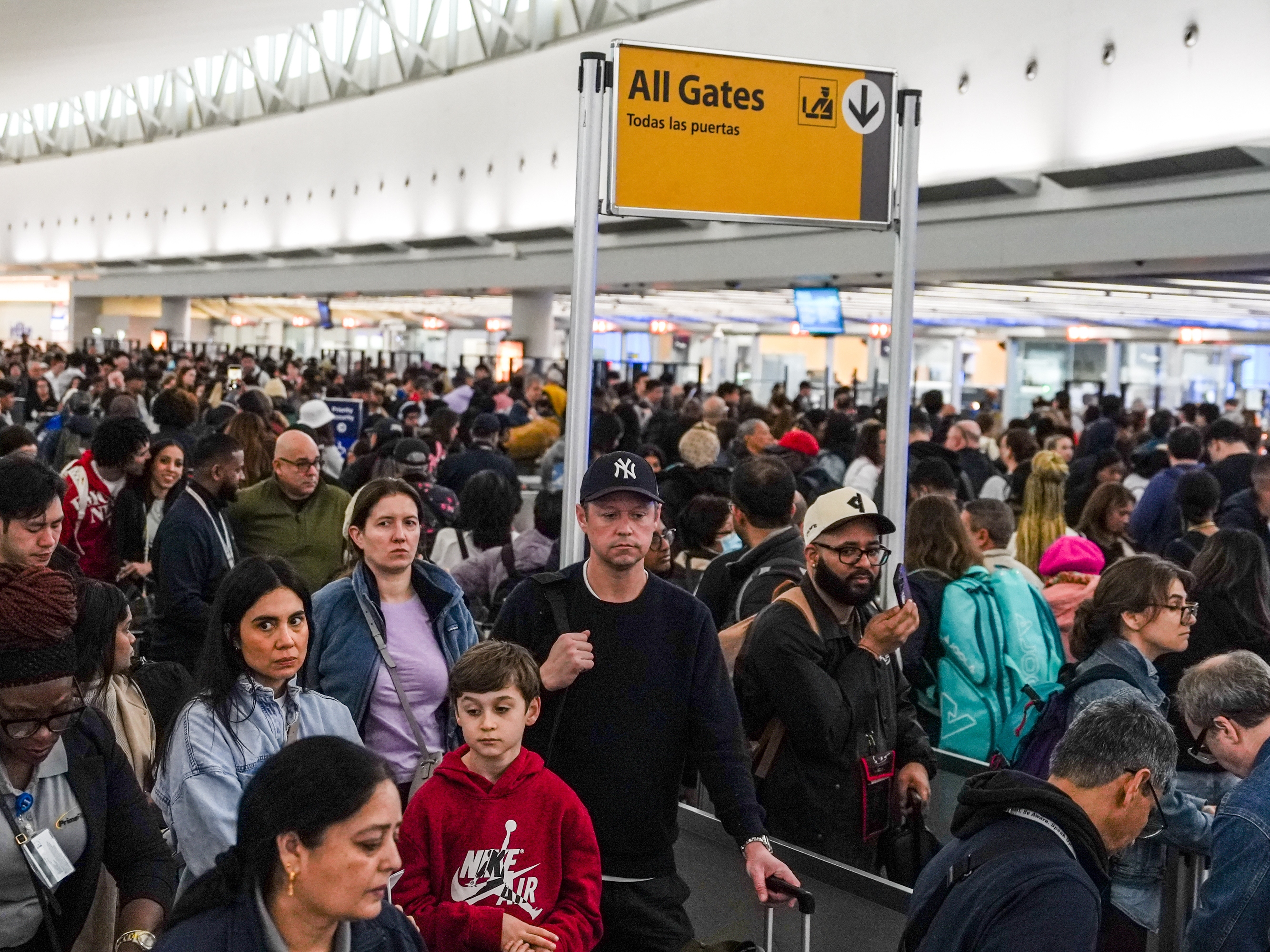 caption: People wait in long TSA security lines at John F. Kennedy International Airport (JFK) in the Queens borough of New York, Monday, March 23, 2026.