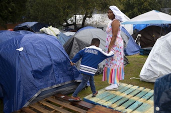 caption: Rita Kuemba of Angola holds hands with her 6-year-old son, Wilson Pedro, while helping to set up tents outside of the Riverton Park United Methodist Church, where nearly 200 people are sheltering while seeking asylum, on Monday, October 16, 2023, in Tukwila. 
