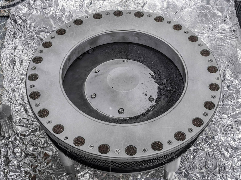caption: Small rocks and dust from an asteroid, outside a round sample collection device in a NASA lab.