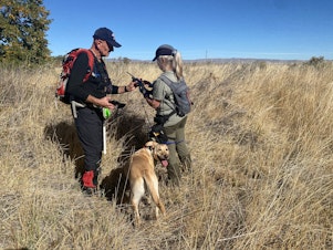 caption: Scott Welton (left), Suzanne Elshult (right), and Kili (center) stand in a field as the group searches for potential remains at Mool-Mool, or Fort Simcoe Historical State Park. 
