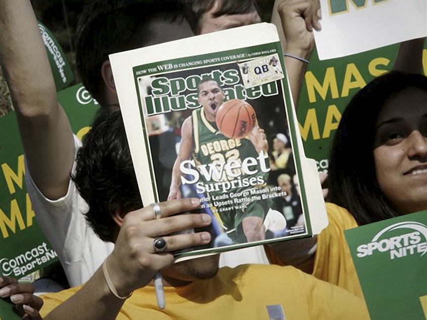 caption: A George Mason University fan holds up the cover of Sports Illustrated magazine at a send-off for the team, on March 29, 2006, in Fairfax, Va. The union representing the magazine's staff said that SI's publisher plans to cut "a significant number, possibly all" of its union-represented staff.