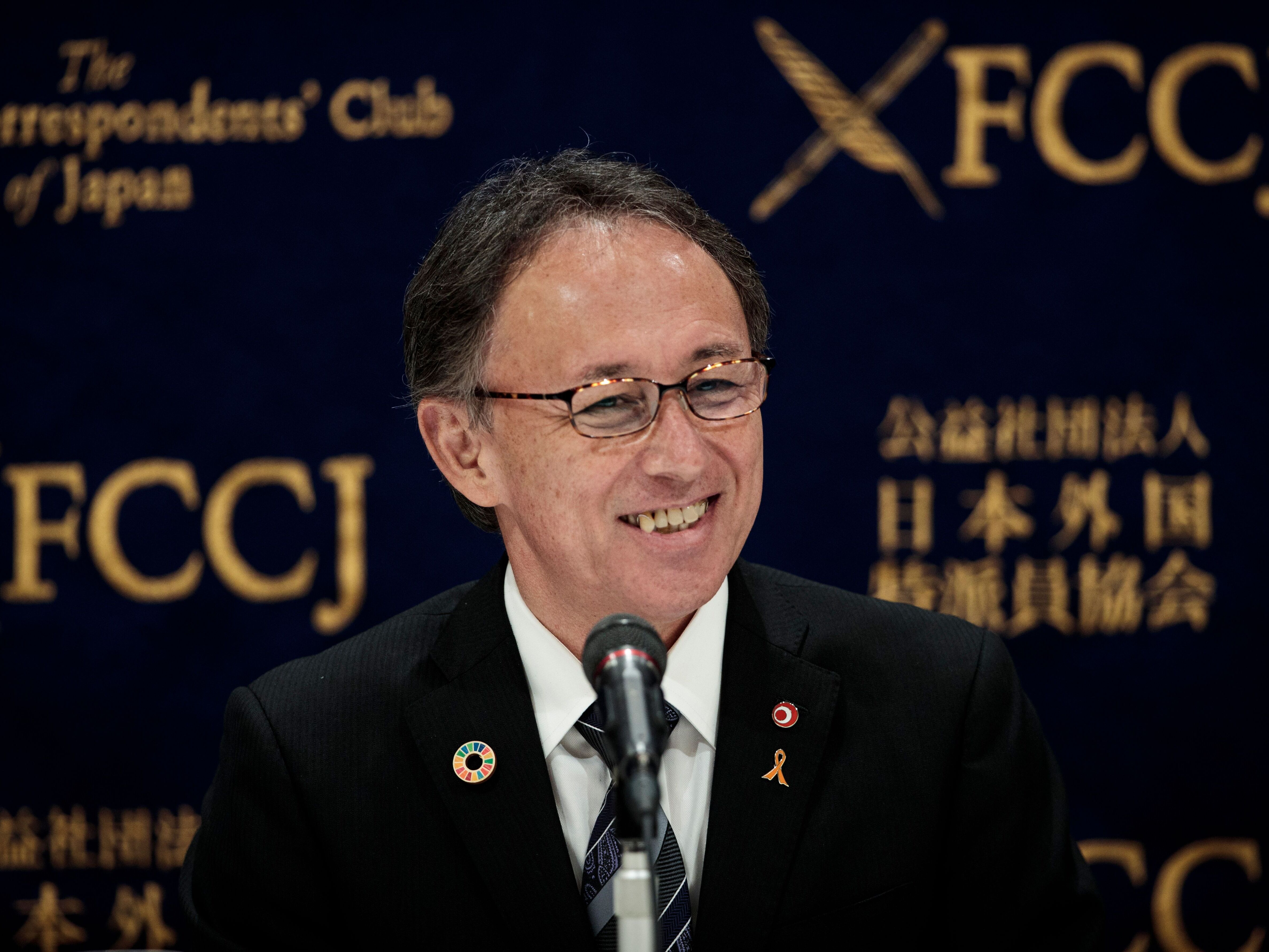 caption: Okinawa Governor Denny Tamaki smiles during a press conference in Tokyo on March 1, 2019, after a vote on the relocation of a U.S. base on the island on Feb. 25.