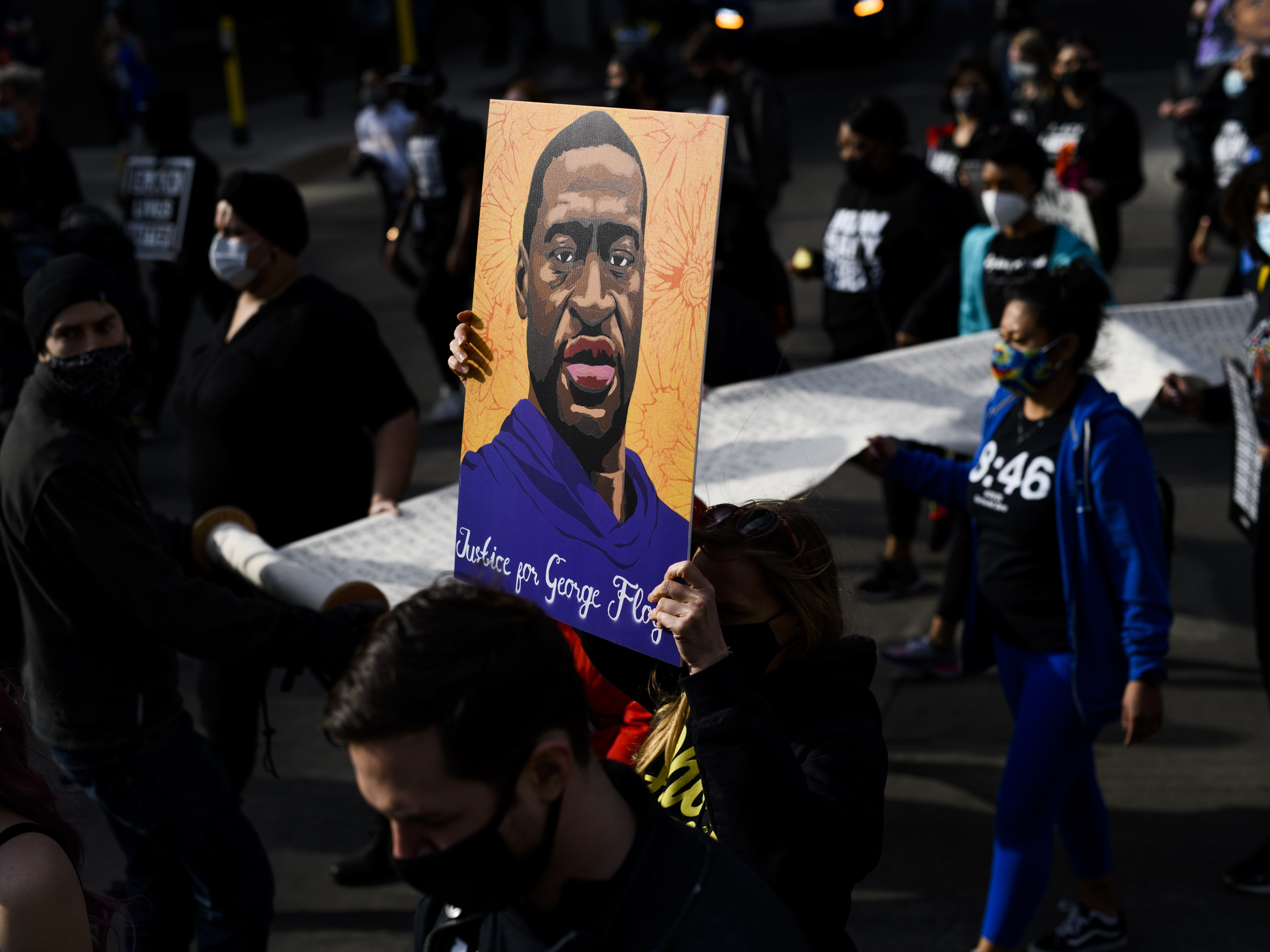 caption: Demonstrators carry a scroll listing the names of people killed by police during a march in honor of George Floyd on March 7, 2021 in Minneapolis, Minnesota.
