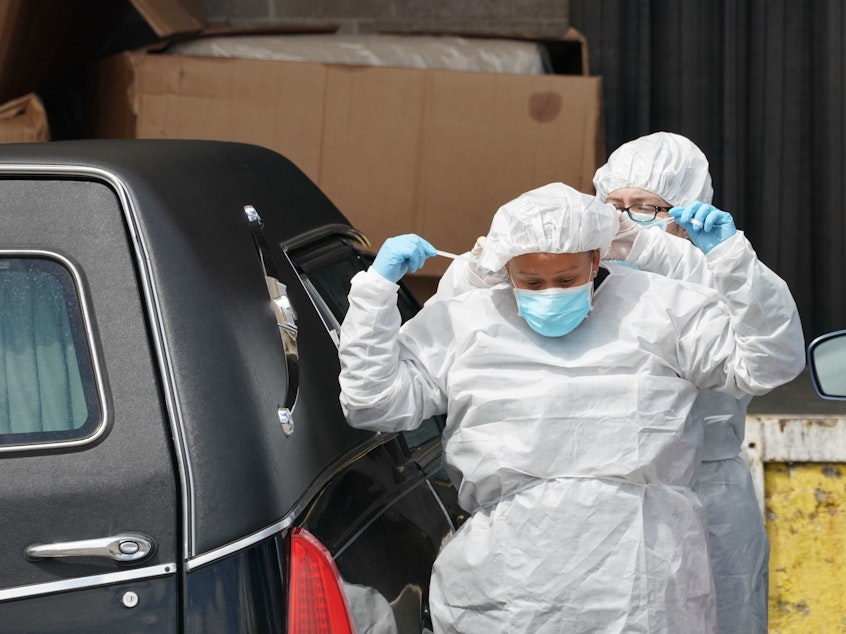 caption: Funeral home workers put on protective gear to retrieve a body from a refrigerated truck outside of a Brooklyn hospital in early April. As of Sunday, the U.S. reported the most coronavirus deaths in the world, surpassing Italy.