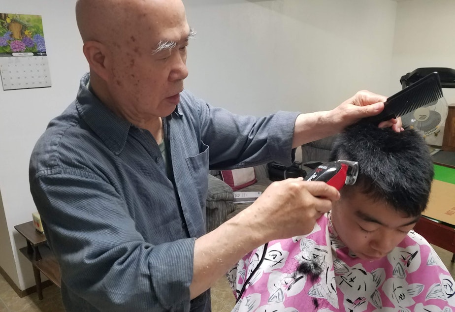 caption: Cho Yuen gives Colin’s little brother a haircut in the barbershop in his basement.
