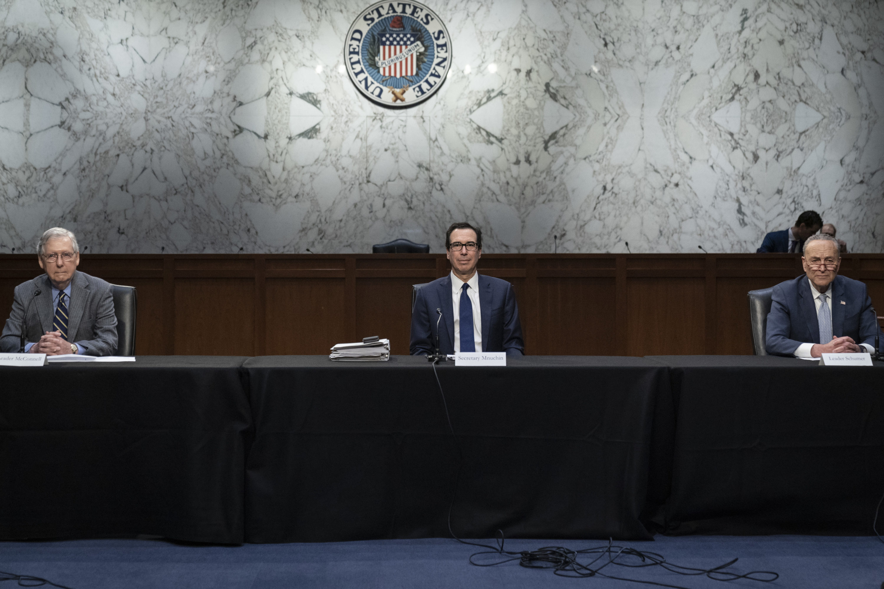 caption: Socially distanced apart, Senate Majority Leader Mitch McConnell (R-KY), U.S. Treasury Secretary Steven Mnuchin, and Senate Minority Leader Chuck Schumer (D-NY) attend a meeting with a select group of Senate Republicans, Senate Democrats, and Trump administration officials in the Hart Senate Office Building on Capitol Hill March 20, 2020 in Washington, DC. (Drew Angerer/Getty Images)