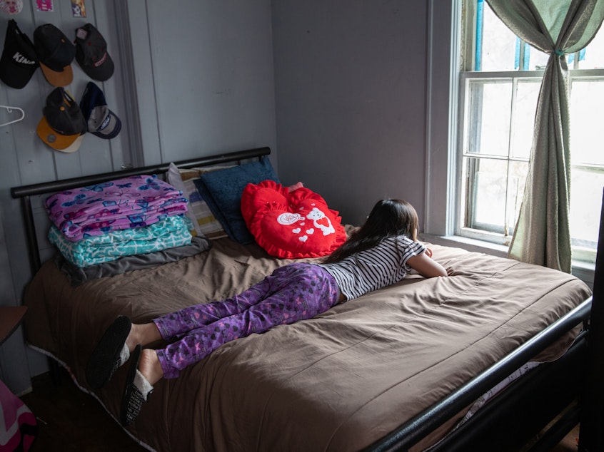caption: A 8-year-old looks out her bedroom window during self-quarantine with her family due to COVID-19.