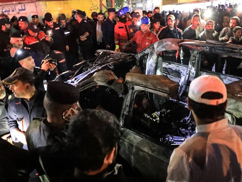 caption: People, rescuers and security forces gather around a vehicle hit by a drone strike, reportedly killing three people, including two leaders of a pro-Iran group, in Baghdad on Wednesday.