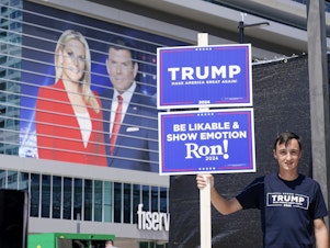 caption: A former president Donald Trump supporter stands near the Fiserv Forum as set up continues for the upcoming Republican presidential debate Tuesday in Milwaukee.