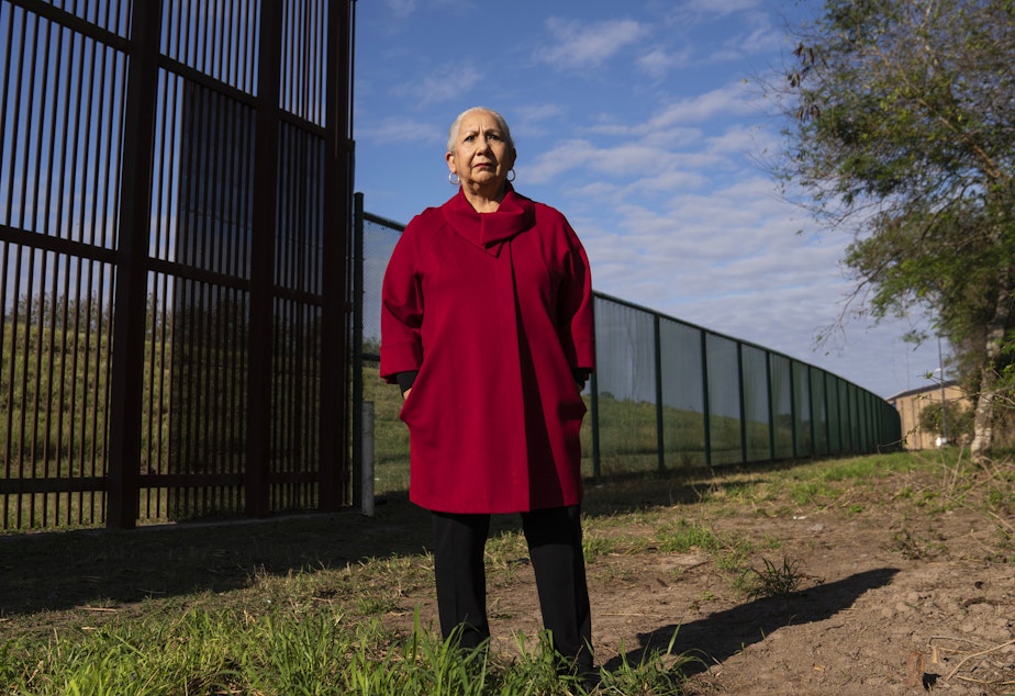 Juliet García, former president of the University of Texas at Brownsville, stands behind the border wall.