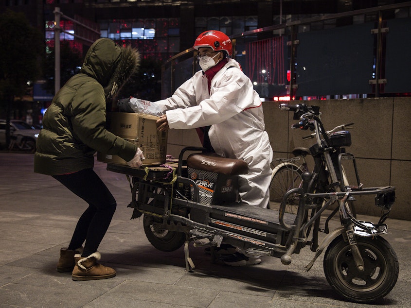 caption: A delivery person wears a protective mask and suit as he delivers packages by bicycle on Saturday in Wuhan, China.