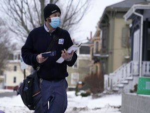 caption: Postal carrier Josiah Morse in Portland, Maine. The USPS is seeking a temporary delay from COVID-19 vaccine requirements.
