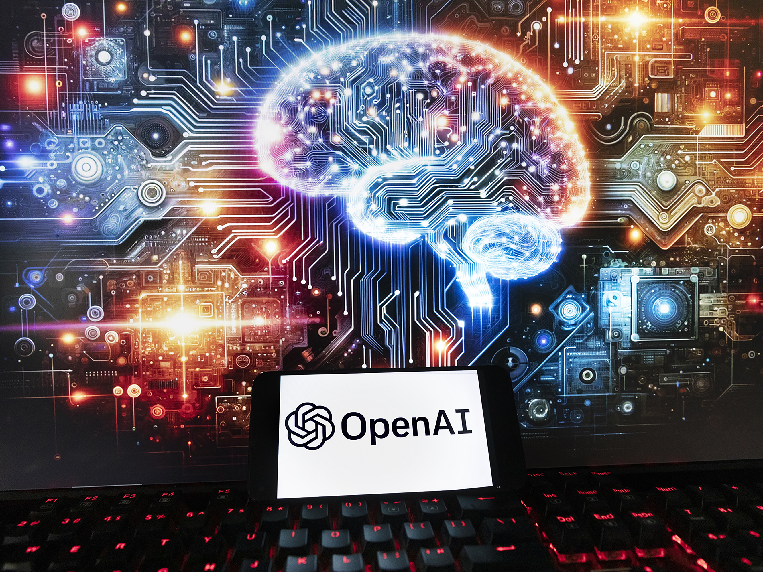 caption: The OpenAI logo is displayed on a cellphone with an image on a computer monitor generated by ChatGPT's Dall-E text-to-image model in Boston on Dec. 8, 2023.