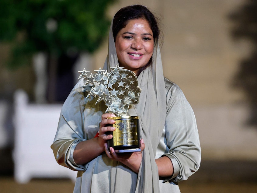 caption: Pakistani teacher Riffat Arif, known as Sister Zeph, is the 2023 winner of the Varkey Foundation Global Teacher Prize. She holds a trophy presented at a dinner in her honor in Paris. She says she faced bad treatment from her teachers at school and dreamed of "a teacher who gives equal respect and love to children with no difference. I could not find that teacher, so I will be that teacher."