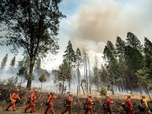 caption: Inmate firefighters battle a California wildfire in July. Qualified inmates can volunteer to be trained in firefighting; in exchange, they are paid $2 a day and an extra $1 per hour when fighting fires. The inmate firefighters also receive sentence reductions.