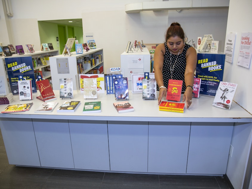 caption: Librarian Sabrina Jesram arranges a display of books during Banned Books Week at a public library branch in New York City on Sept. 23, 2022. 
