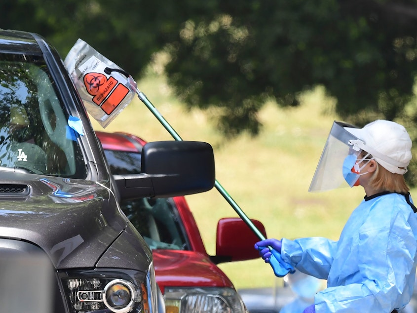 caption: A coronavirus test kit is handed to a driver in a vehicle at a testing site in Los Angeles on Wednesday.