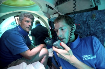 caption: Submersible pilot Randy Holt, right, communicates with the support boat as he and Stockton Rush, left, CEO and Co-Founder of OceanGate, dive in the company's submersible, "Antipodes," about three miles off the coast of Fort Lauderdale, Fla., June 28, 2013. Rescuers are racing against time to find the missing submersible carrying five people, who were reported overdue Sunday night, June 18, 2023.